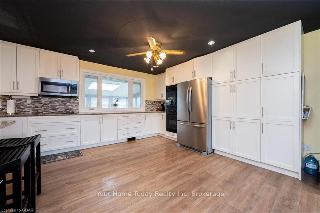 Kitchen with tasteful backsplash, white cabinetry,